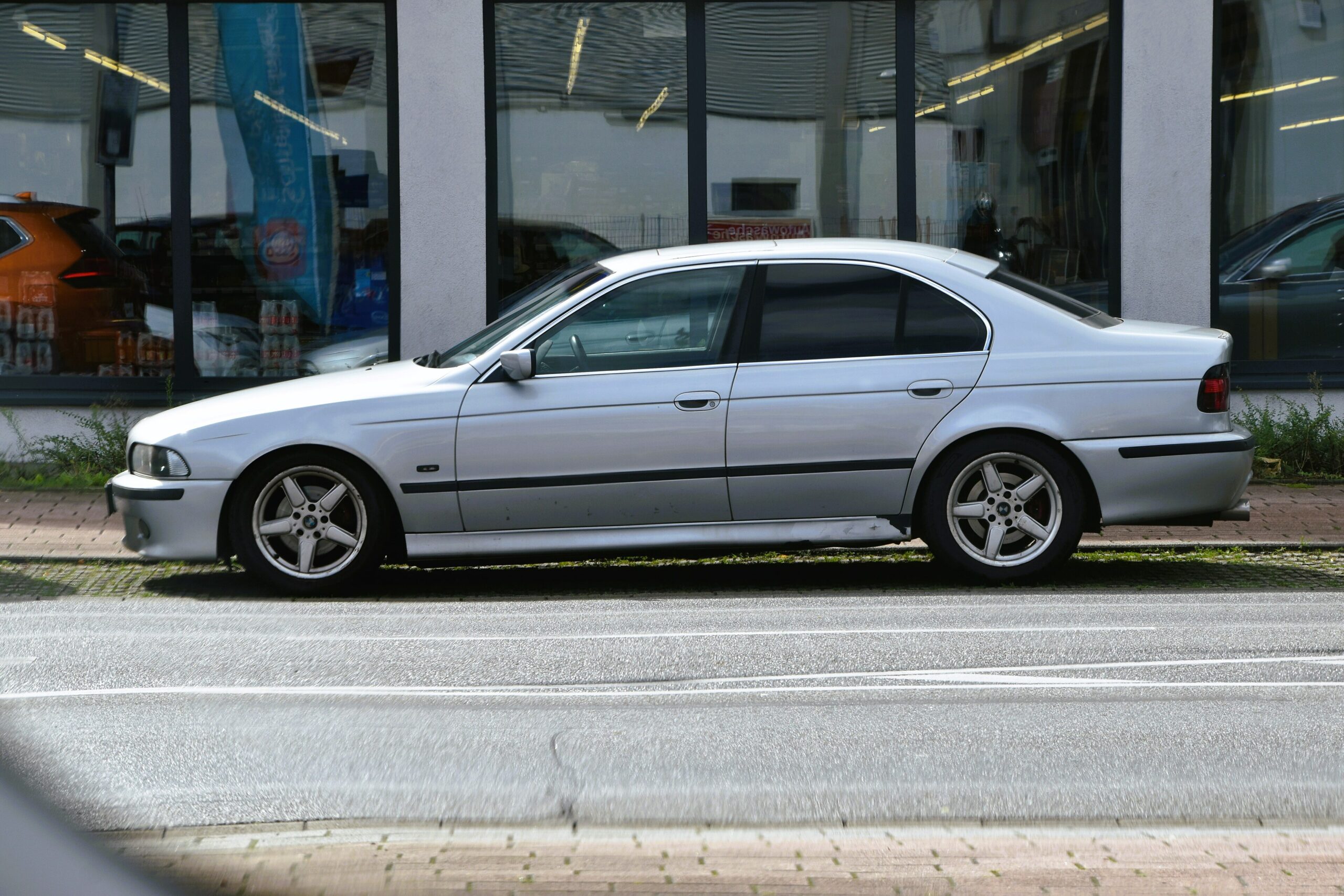 Silberner BMW 520i der Baureihe E39 in Seitenansicht vor einer Glasfassade