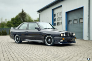 Dunkelblauer BMW M3 E30 Cecotto in Seitenansicht vor einer Werkstatthalle