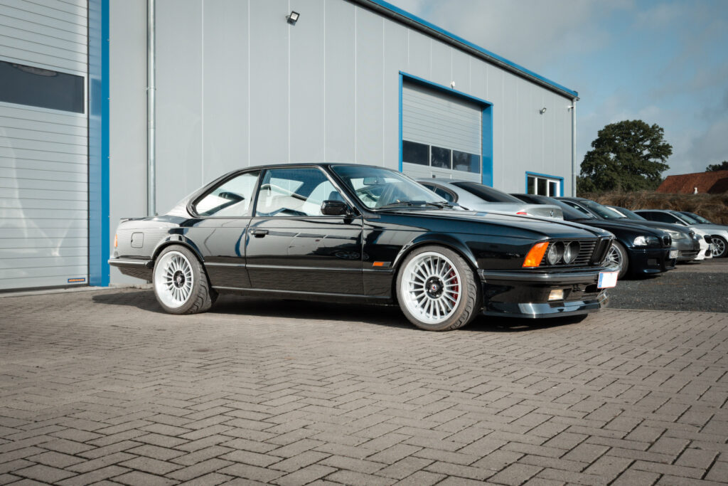 Schwarzer BMW M635 CSi der Baureihe E24 schräg von vorn rechts vor einer Halle