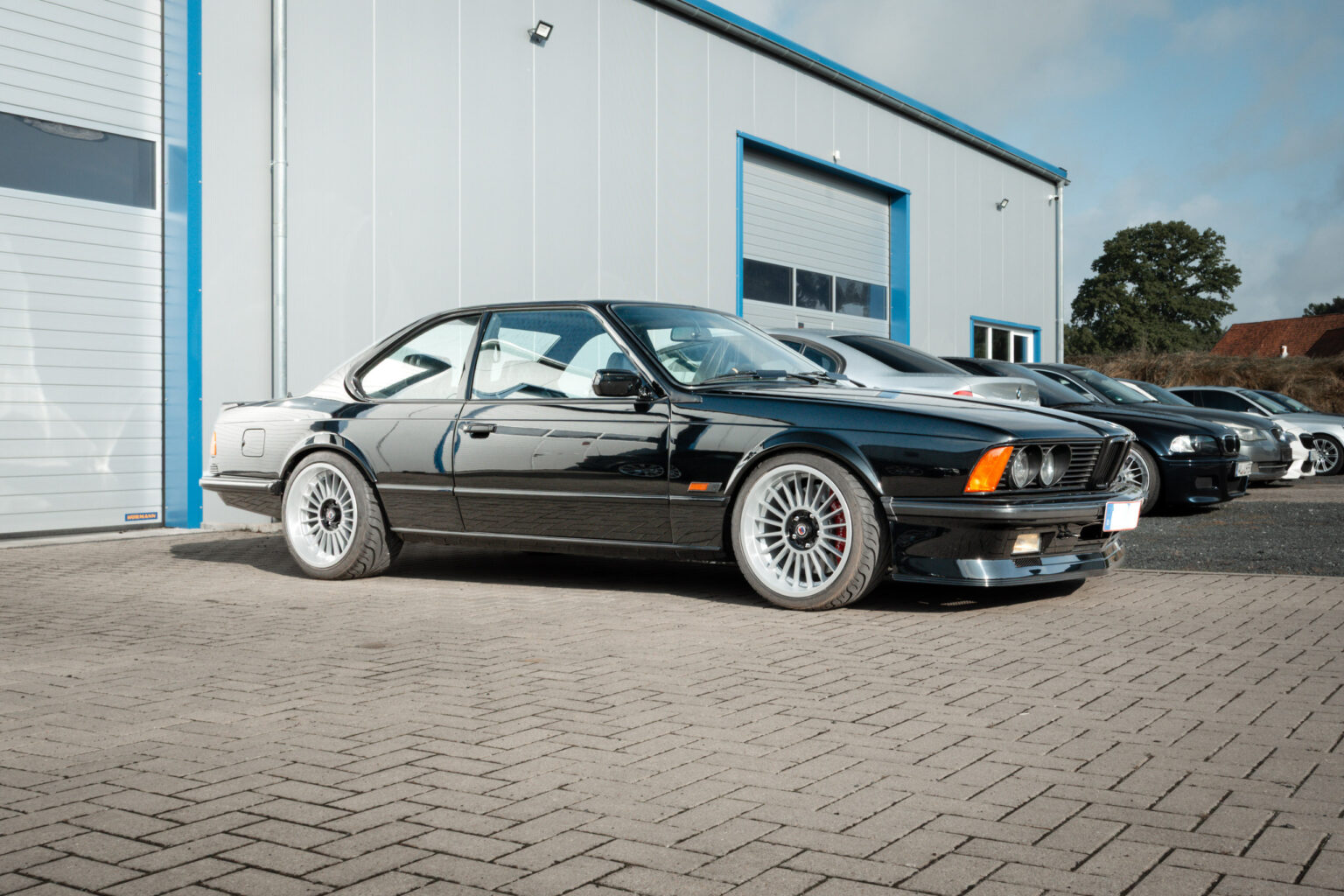 Schwarzer BMW M635 CSi der Baureihe E24 im Profil vor einer Werkstatthalle