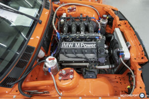 Rennversion des BMW S14 mit Einzeldrosselklappen und Kohlefaser-Ansaugtrichtern im Motorraum eines orangefarbenen BMW M3 E30