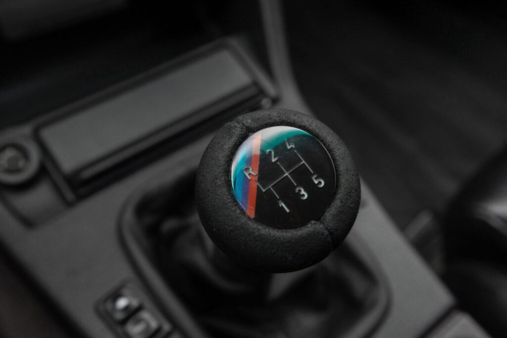 BMW M3 E30 Sport Evolution in Mauritiusblau (AC79200) — Schaltknauf mit M-Farben und Schaltschema in Wildleder
