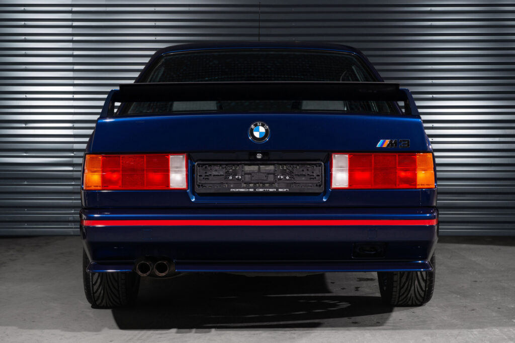 BMW M3 E30 Sport Evolution in Mauritiusblau (AC79200) — Heckansicht mit Rückleuchten, Doppelendrohr und rotem Heckstreifen