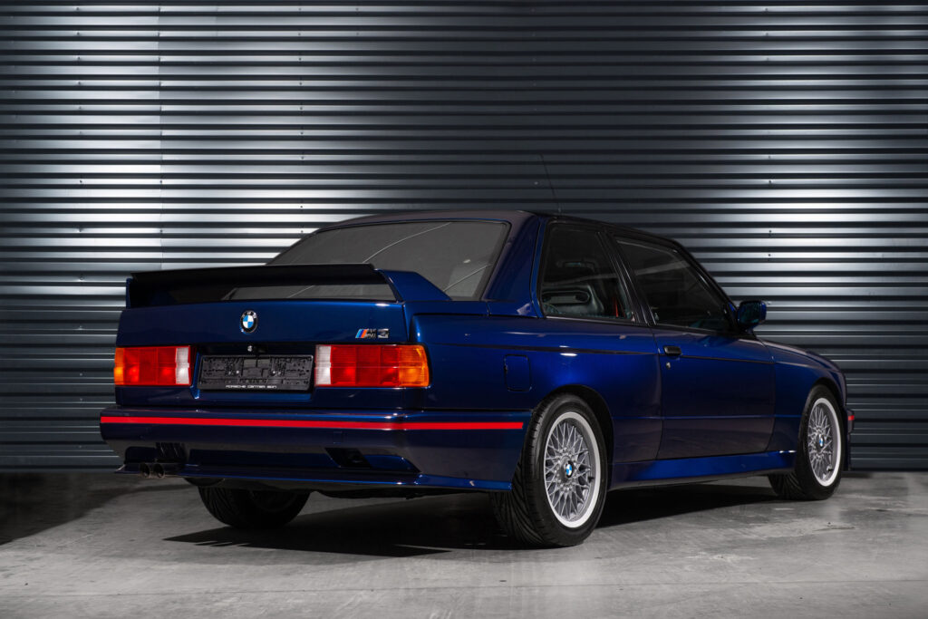 BMW M3 E30 Sport Evolution in Mauritiusblau (AC79200) — Heckansicht von schräg hinten mit Heckflügel und BBS-Kreuzspeichenfelgen