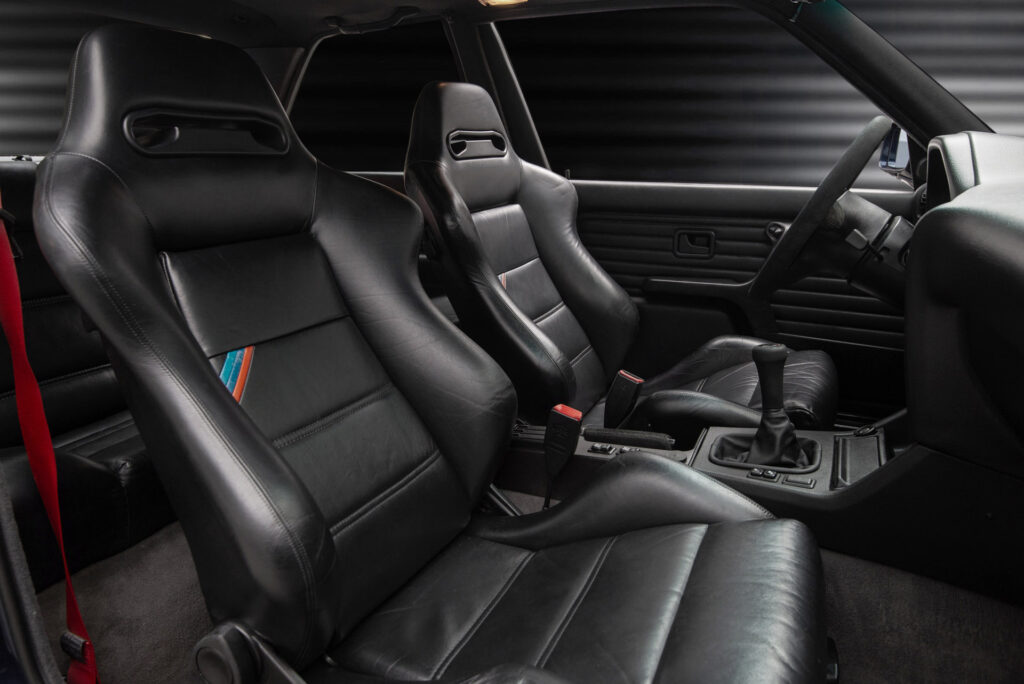 BMW M3 E30 Sport Evolution in Mauritiusblau (AC79200) — Blick durch die Beifahrertür auf beide Ledersitze mit M-Streifen