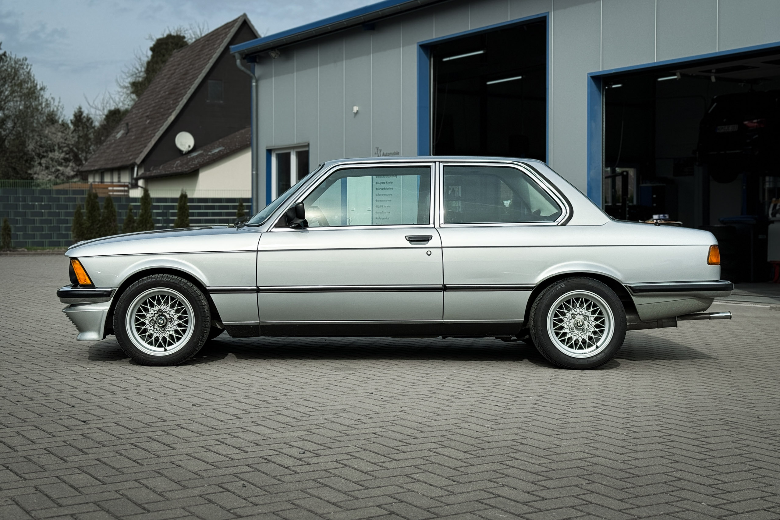 BMW 323i der Baureihe E21 in Polarsilber, Seitenansicht vor einer Werkstatt