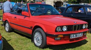 Rotes BMW 325i Cabriolet der Baureihe E30 auf einer Treffen-Wiese