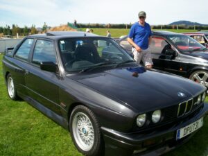 Schwarzer BMW M3 der Baureihe E30 in Dreiviertelansicht von vorn rechts, mit verbreiterten Kotflügeln und Heckflügel