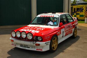 BMW M3 E30 Gruppe A Rallyewagen in roter Bastos-Lackierung mit Zusatzscheinwerfern, Frontansicht